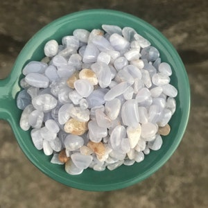 Puede incluir: Un bol lleno de piedras de &aacute;gata azul lazada pulidas. Las piedras son de color azul claro con marcas blancas y marrones.