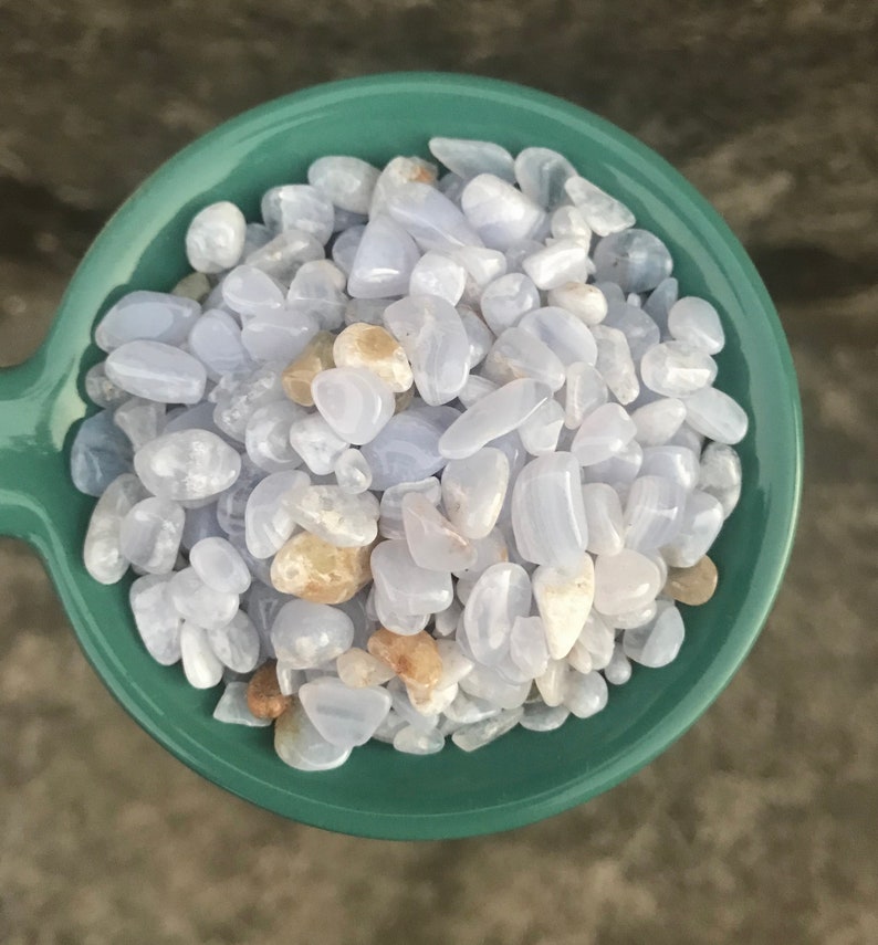 Puede incluir: Un bol lleno de piedras de &aacute;gata azul lazada pulidas. Las piedras son de color azul claro con marcas blancas y marrones.