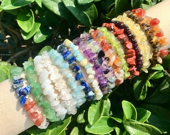 Op de afbeelding: Een set van 12 armbanden gemaakt van verschillende halfedelstenen, waaronder amethist, aquamarijn, carneol, helder kwarts, citrien, groene aventurijn, lapis lazuli, rode jaspis, tijgeroog en witte howliet. De armbanden zijn gestapeld op een wit oppervlak.