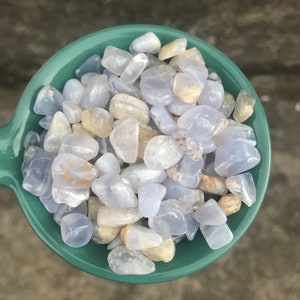 Puede incluir: Primer plano de un cuenco de color turquesa lleno de piedras de &aacute;gata azul y blanca pulidas. Las piedras son lisas y pulidas, con una variedad de formas y tama&ntilde;os.