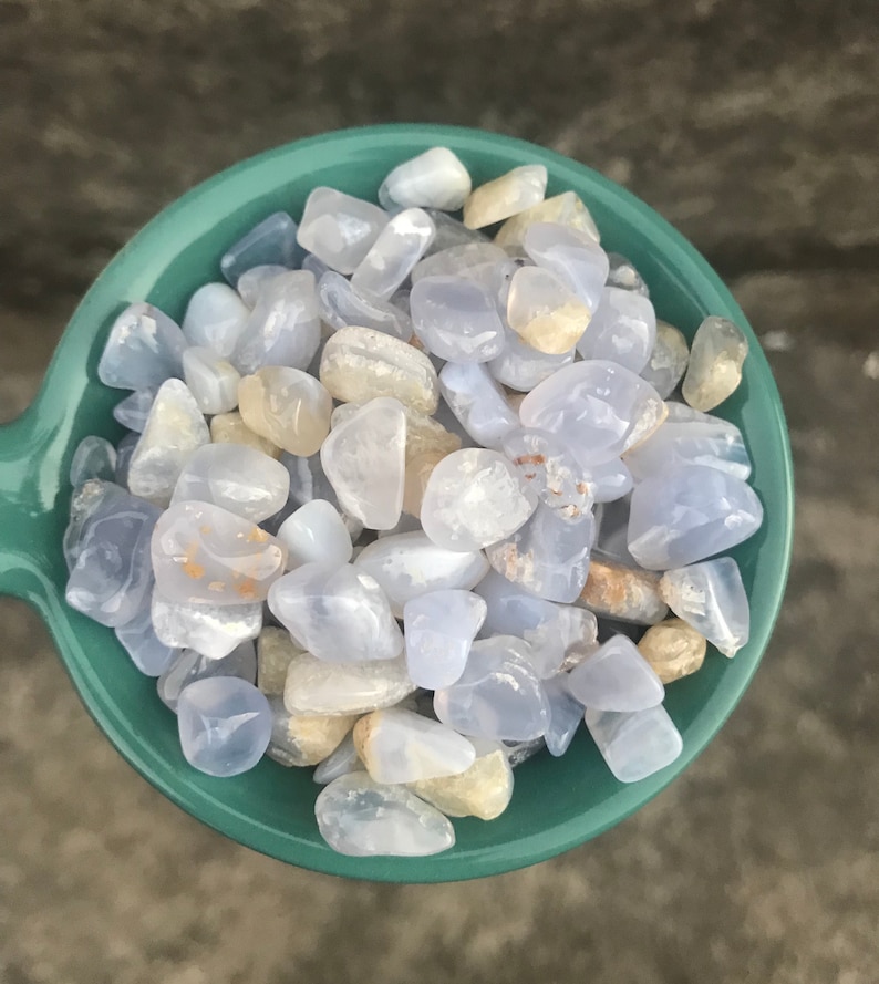 Puede incluir: Primer plano de un cuenco de color turquesa lleno de piedras de &aacute;gata azul y blanca pulidas. Las piedras son lisas y pulidas, con una variedad de formas y tama&ntilde;os.