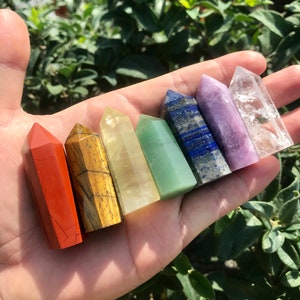 Op de afbeelding: Zeven chakra-kristalpunten in een regenboog van kleuren, waaronder rood, oranje, geel, groen, blauw, indigo en violet. De punten zijn in een rij gerangschikt, met de rode punt links en de violette punt rechts.