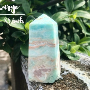 May include: A large, light blue and white aquamarine crystal point, measuring 3-3.5 inches tall. The crystal has a layered, banded pattern with hints of pink and brown.