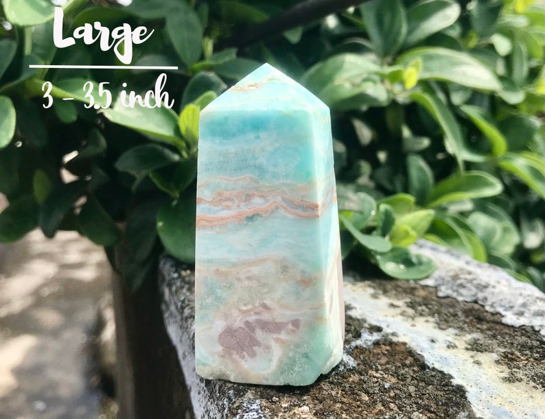 May include: A large, light blue and white aquamarine crystal point, measuring 3-3.5 inches tall. The crystal has a layered, banded pattern with hints of pink and brown.