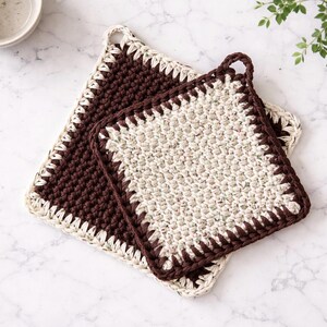 May include: Two square crochet potholders. One is dark brown with a cream border, and the other is cream with a dark brown border. Both have a loop for hanging. The potholders are handmade and have a textured appearance.