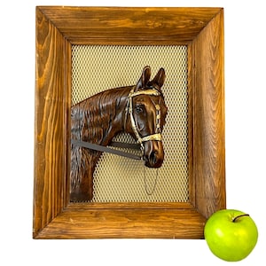 May include: A wooden framed wall decor featuring a brown horse head sculpture with a gold bridle. The sculpture is mounted on a gold mesh background.