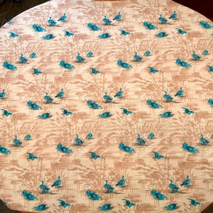 May include: A beige oval tablecloth with a repeating pattern of blue ducks swimming in a pond with brown reeds.