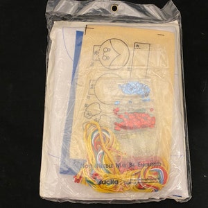May include: A craft kit with a white fabric base, colorful embroidery floss, and a pattern for creating a beaded design. The kit includes instructions and a needle. The packaging includes the text "Note: Needle May Be Enclosed".