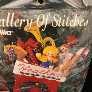 May include: A Bucilla Gallery of Stitches stocking kit featuring a red stocking with a green holly wreath, a gingerbread man, a toy soldier, a doll, a rocking horse, and a trumpet. The stocking is personalized with the name "Heather".
