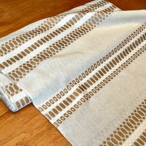 May include: White fabric with a brown geometric pattern. The pattern is made up of small ovals and squares.