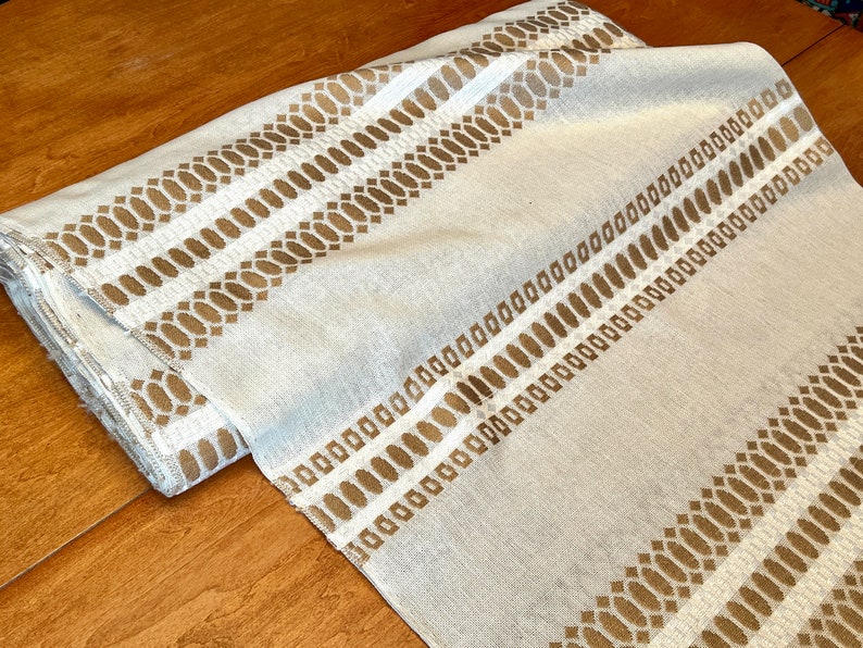 May include: White fabric with a brown geometric pattern. The pattern is made up of small ovals and squares.