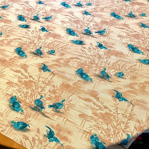 May include: A vintage tablecloth with a repeating pattern of blue ducks swimming in a pond with brown reeds. The background is a light beige color.