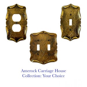 Puede incluir: Juego de tres placas de interruptor de latón de estilo antiguo. Incluye una cubierta de toma doble, una cubierta de interruptor simple y una cubierta de interruptor doble. Las placas tienen un aspecto texturizado y envejecido y un diseño ornamental. El texto "Amerock Carriage House Collection: Your Choice" está en la parte inferior.