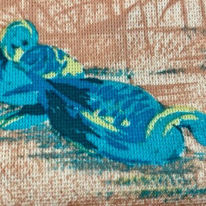 May include: A close-up of a blue and green floral pattern on a light brown fabric. The pattern is of a bird with its head tucked under its wing.