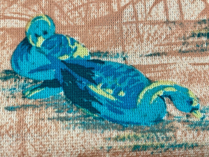May include: A close-up of a blue and green floral pattern on a light brown fabric. The pattern is of a bird with its head tucked under its wing.