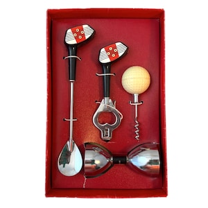 May include: A bar tool set in a red box containing a long-handled spoon, a bottle opener, a corkscrew with a golf ball handle, and a double-sided jigger. The spoon and bottle opener feature golf club head handles with red, white, and black details.
