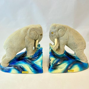 May include: A pair of gray ceramic elephant bookends standing on blue and white waves. The bookends are made by Toronto Canada.