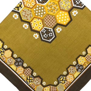 May include: A square fabric cloth featuring an olive green background with a border of interconnected hexagons. Each hexagon contains distinct patterns including white polka dots, yellow flowers, and brown grids, accented by small white floral motifs.