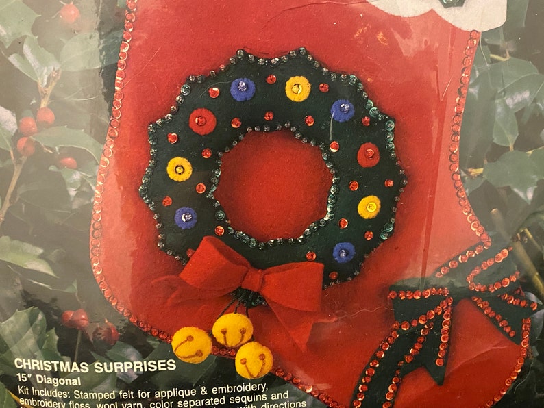 May include: A red felt stocking with a green felt wreath decorated with colorful sequins and buttons. The stocking also has a red felt bow and three yellow felt bells.