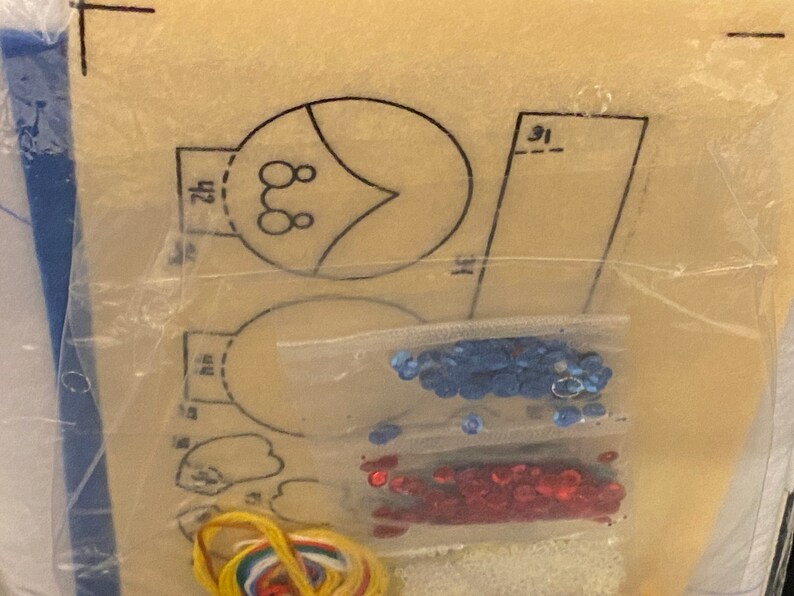 May include: A craft kit with a pattern for making a felt ornament. The kit includes blue and red sequins, yellow embroidery floss, and a white felt sheet.