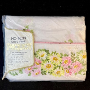 May include: A white double flat sheet with a pink and yellow floral print. The sheet is packaged in plastic and has a label that reads "NO-IRON luxury muslin PEQUOT 80% DACRON POLYESTER 50% COTTON/COTON DOUBLE FLAT SHEET FOR 54" IN MATTRESS SEAM IN BEFORE HEMMING".