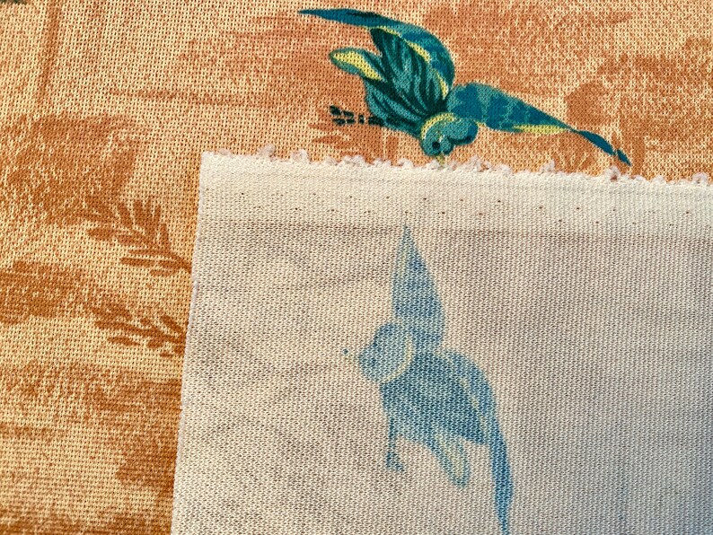 May include: Two fabric swatches, one with a brown background and a blue bird design, and the other with a white background and a blue bird design.