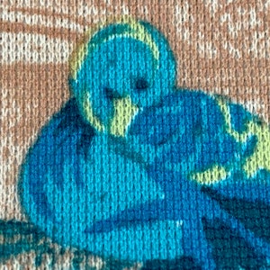May include: Close-up of a brown fabric with a blue and green bird pattern. The fabric has a knitted texture.