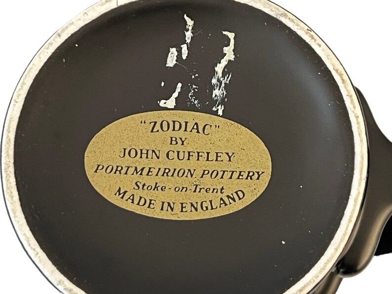 K&ouml;nnte beinhalten: Nahaufnahme des Bodens einer schwarzen Keramiktasse mit einem goldenen Etikett mit der Aufschrift "ZODIAC" von John Cuffley, Portmeirion Pottery, Stoke-on-Trent, Hergestellt in England.