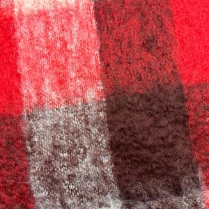 May include: Close-up of a red, black, and gray plaid fabric. The fabric has a fuzzy, textured appearance. The pattern is a classic check design, with large, irregular squares of color.