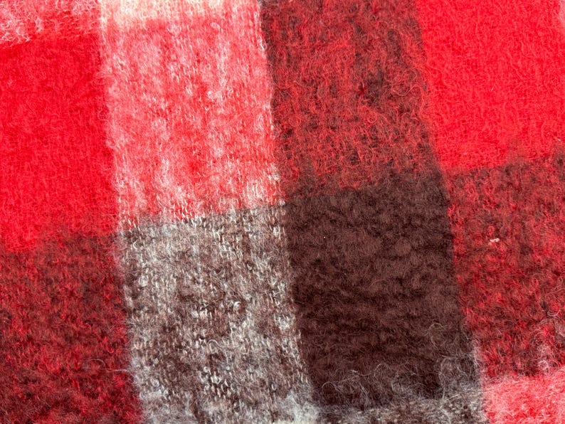 May include: Close-up of a red, black, and gray plaid fabric. The fabric has a fuzzy, textured appearance. The pattern is a classic check design, with large, irregular squares of color.