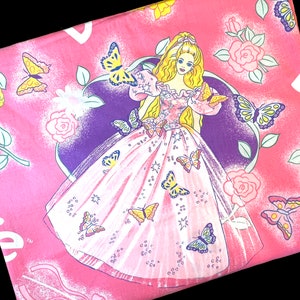 May include: Pink fabric with a princess doll wearing a pink and white dress with butterflies and stars. The background is pink with roses and butterflies.