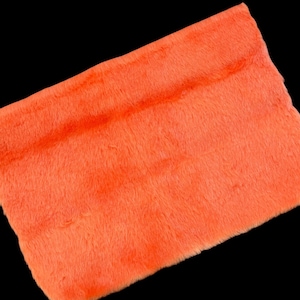 Puede incluir: Una pieza rectangular de piel sintética de color naranja brillante con una textura suave y afelpada. El material presenta un pelo denso y largo que crea una apariencia de color sólido y vibrante en toda la superficie de la pieza textil.