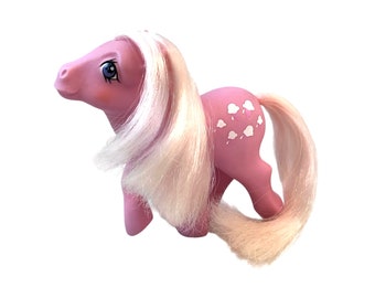 May include: A vintage pink toy pony with white hair and tail. The pony has blue eyes and white cloud-shaped designs on its side. The toy is a collectible item, likely from the 1980s or early 1990s.