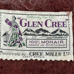 May include: A rectangular white label with the text "Galloway for Glen Cree" in purple and green. The label features an illustration of a person in a kilt and mountains. The label reads "100% Mohair Made in Scotland" and "Manufactured by Cree Mills Ltd Great Britain."