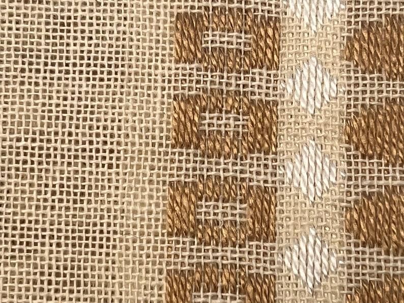 May include: Close-up of a woven fabric with a brown and white pattern. The fabric has a rough texture and a natural look.