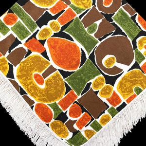 May include: A square, patterned textile with a black background and an abstract design in orange, brown, green, and yellow. The edges are trimmed with a white fringe. The design features geometric shapes and organic forms.