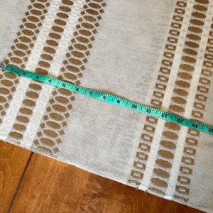 May include: A beige fabric with a brown geometric pattern. A measuring tape is laid across the fabric, showing a measurement of 17 inches.