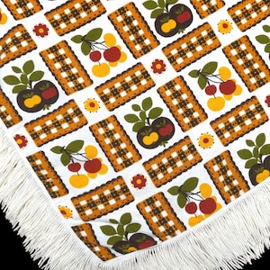 May include: White tablecloth with a brown and white checked pattern and a repeating design of green leaves and red, orange, and yellow fruit. The tablecloth has a white fringe border.