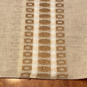 May include: A beige fabric with a brown and white woven pattern. The pattern features a series of squares and circles.