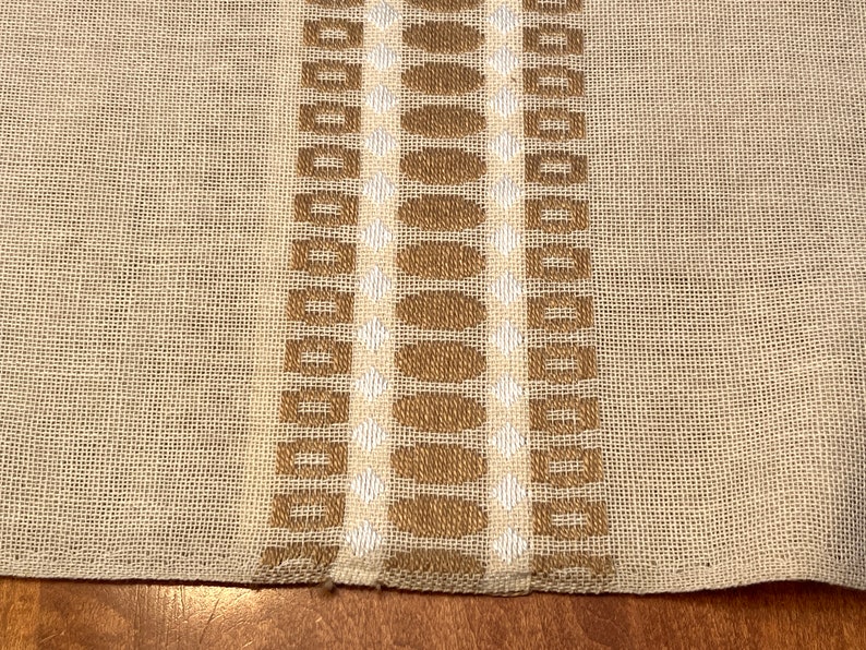 May include: A beige fabric with a brown and white woven pattern. The pattern features a series of squares and circles.