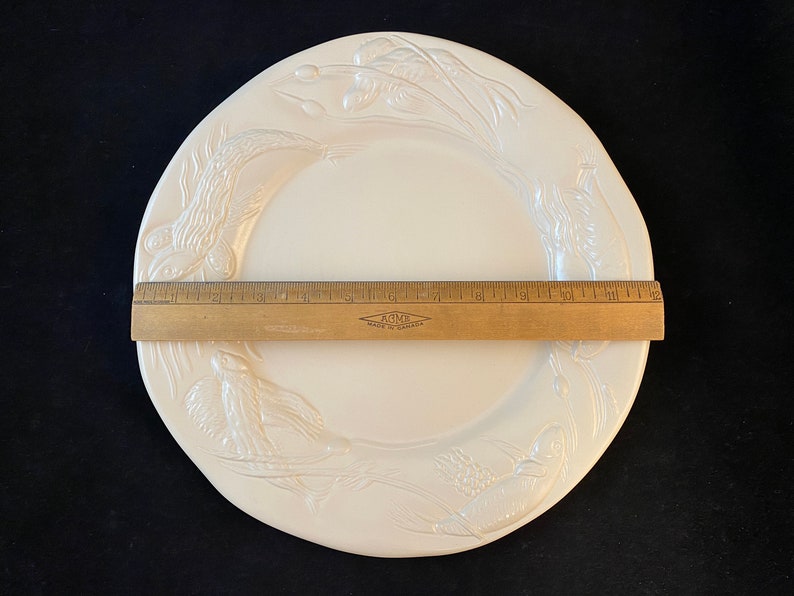 K&ouml;nnte beinhalten: Wei&szlig;er Keramik-Dinnerteller mit einem erhabenen Design aus V&ouml;geln und Weizen. Der Teller hat einen Durchmesser von 25,4 cm.