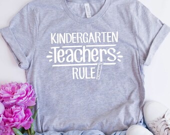 May include: Gray t-shirt with white text that reads "Kindergarten Teachers Rule" with a ruler graphic.