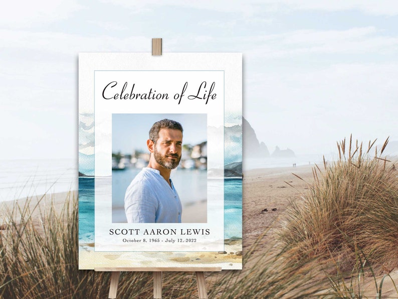 May include: A white sign with a watercolour background of blue and white waves. The sign says "Celebration of Life" and features a photo of a man with a beard. The text below the photo reads "Scott Aaron Lewis, October 8, 1965 - July 12, 2022".