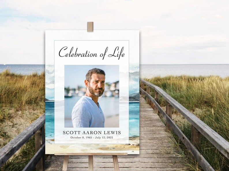 May include: A white sign with a blue watercolour background featuring a beach scene. The sign reads "Celebration of Life" and includes a photo of a man. The text below the photo reads "Scott Aaron Lewis, October 8, 1965 - July 12, 2022".