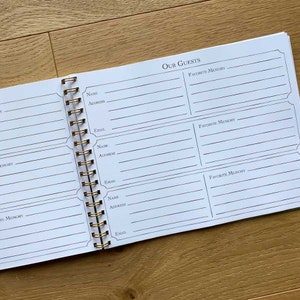 May include: A white spiral bound guest book with the title "Our Guests" printed at the top. The book has spaces for guests to write their names, addresses, emails, and favorite memories.
