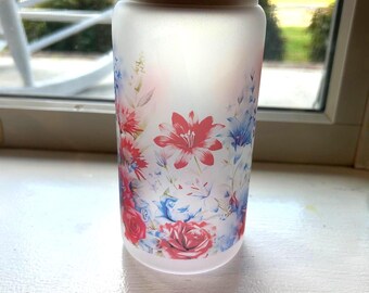 Vaso de vidrio esmerilado con flores rojas, blancas y azules con pajita