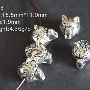 Pode incluir: Cinco contas de prata com forma de cabeça de lobo com entalhes detalhados. As contas medem 15,5 mm por 11,0 mm e têm um furo de 1,9 mm. PA03.