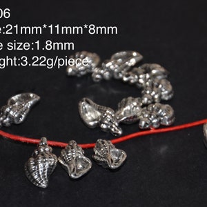 Könnte beinhalten: Silberne Muschel-Anhänger mit einem Loch zum Aufziehen. Die Anhänger sind ca. 21 mm x 11 mm x 8 mm groß und haben ein 1,8 mm Loch. CO06.