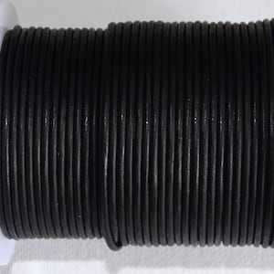 Può includere: Un rotolo di cordoncino in pelle nera, avvolto strettamente attorno a un rotolo di plastica bianca.