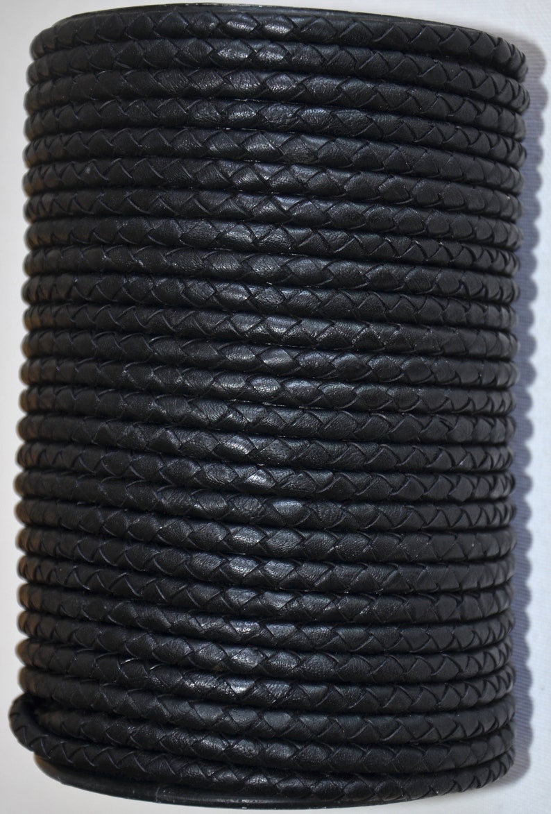 Puede incluir: Un rollo de cord&oacute;n de cuero trenzado negro. El cord&oacute;n est&aacute; enrollado firmemente, creando una forma cil&iacute;ndrica. La textura del cuero es visible, con un patr&oacute;n de hebras entrelazadas. La apariencia general es elegante y oscura.